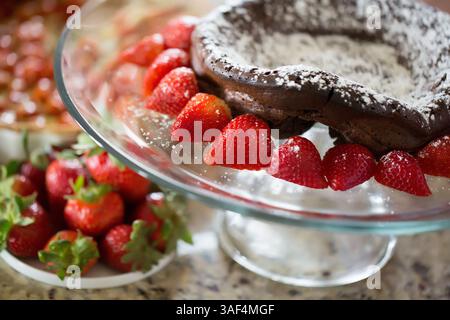 Torta al cioccolato con zucchero a velo e fragole su supporto di vetro. Foto Stock