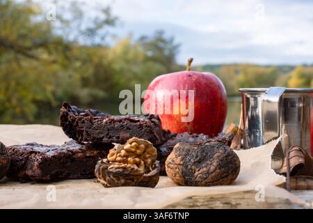Picnic sul lago tranquillo. Tazza di metallo con caffè caldo o tee sul molo di legno sul tranquillo lago. Paesaggio naturale autunnale. Mele rosse, foglie autunnali, Foto Stock