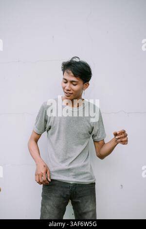 Giovane uomo asiatico con un abbigliamento casual in piedi su un semplice sfondo bianco mentre indossa una t-shirt grigia Foto Stock