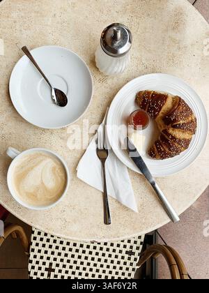Vista dall'alto di una tipica colazione francese, un croissant con marmellata, burro e cappuccino Foto Stock