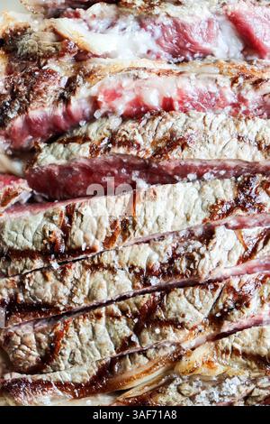 Un primo piano estremo di una bistecca perfettamente cotta e affettata con marmorizzazione grassa visibile e sale marino grezzo, che mostra una consistenza appetitosa Foto Stock