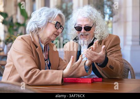 Felice coppia senior caucasica che si scambia un regalo in un caffè all'aperto momento gioioso. Foto Stock
