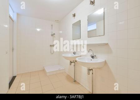 Un bagno semplice e moderno con due lavandini, eleganti specchi e pareti piastrellate. Il design enfatizza la pulizia e la funzionalità. Foto Stock