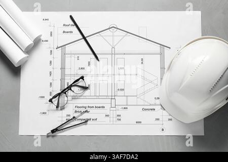 Diversi disegni architettonici, elmetto, matita, divisore e vetri su tavolo grigio, piatto Foto Stock