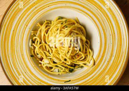 Una porzione splendidamente placcata di spaghetti aglio e olio, guarnita con prezzemolo fresco e aglio a fette sottili. La pasta risplende di olio d'oliva e h Foto Stock