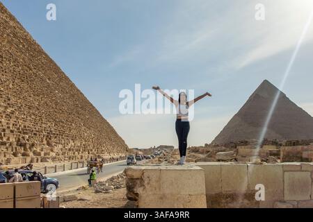 Cairo, Egitto; 20 gennaio 2024: Osserva una bella donna in posa tra le famose piramidi di Giza in Egitto, che si collega con gli antichi spiriti di Myce Foto Stock
