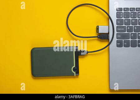 Laptop con unità flash, disco rigido esterno su sfondo giallo. Ripresa in studio, vista dall'alto. Foto Stock