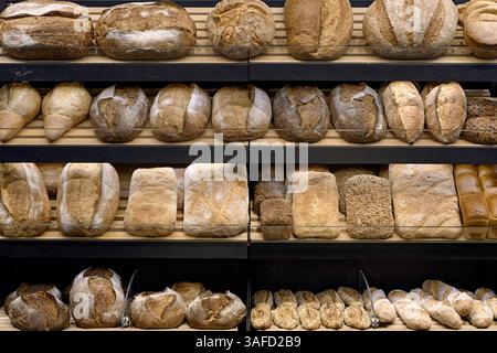 Vari tipi di pane tradizionale fatto in casa sugli scaffali in legno di un negozio di panetteria e sullo sfondo di una panetteria astratta Foto Stock
