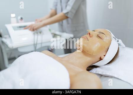 Donna che riceve un trattamento maschera viso ringiovanente in un salone di bellezza professionale per l'idratazione della pelle. Foto Stock