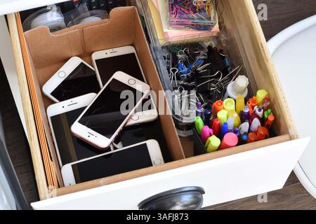 4 aprile 2025 - Newmarket, Ontario, Canada: Una collezione di vecchi iPhone obsoleti rotti all'interno di un cassetto spazzatura, che illustrano i rifiuti tecnologici Foto Stock