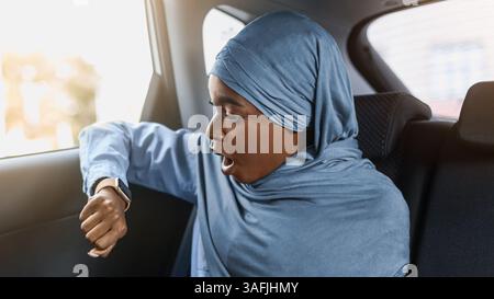 Essere in ritardo. Stressed Businesswoman musulmano nero seduta in taxi e tempo di controllo Foto Stock
