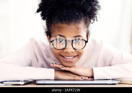 Ritratto di una ragazza preadolescente africana in posa seduta alla scrivania al coperto Foto Stock