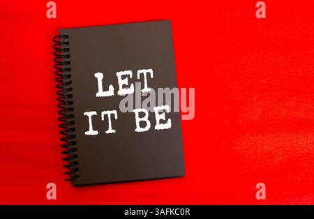 Lasciare che sia scritto su una pagina nera del notebook su sfondo rosso. Concettuale che sia simbolo. Copia spazio. Foto Stock