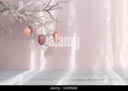 Uova di Pasqua appese al ramo su sfondo rosa pastello Foto Stock