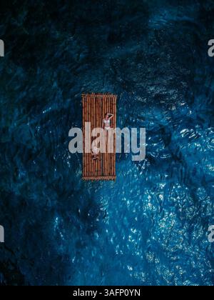 Vista aerea di una zattera di bambù che galleggia sull'oceano blu profondo con due persone che si rilassano Foto Stock