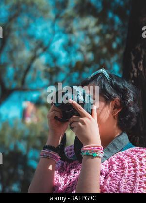 Fotografa donna con una fotocamera professionale, sta scattando una foto nel parco concentrandosi su qualcosa, il concetto di giorno del fotografo. Foto Stock