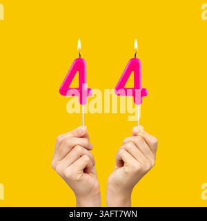 Mani che tengono le candele di compleanno con il numero 44 - sfondo giallo Foto Stock
