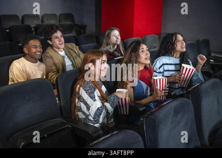 Gruppo di amici entusiasti che si godono un film e mangiano popcorn al cinema, condividendo un'esperienza divertente e divertente Foto Stock