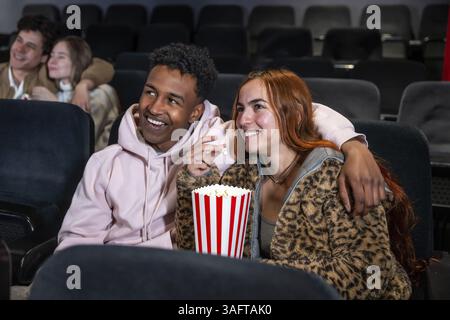 Coppia felice che condivide popcorn mentre guarda un film al cinema, trascorrendo una serata fuori con gli amici Foto Stock
