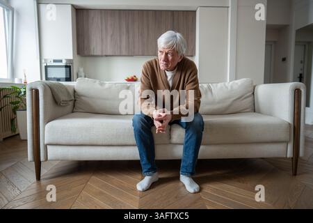 Uomo anziano abbandonato solo si siede perso nel pensiero sul divano con le braccia incrociate, perdita di memoria depressa Foto Stock