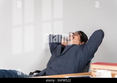 Calmo uomo millenario con gli occhiali sedersi rilassarsi a casa, ufficio, fare un pisolino o sognare ad occhi aperti. Felice rilassato caucasico giovane maschio riposo in sedia distratto fr Foto Stock