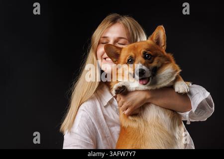 Giovane donna felice che abbraccia il suo carino cane gallese Corgi, sorridente e godendo un momento di gioia in studio. Foto Stock