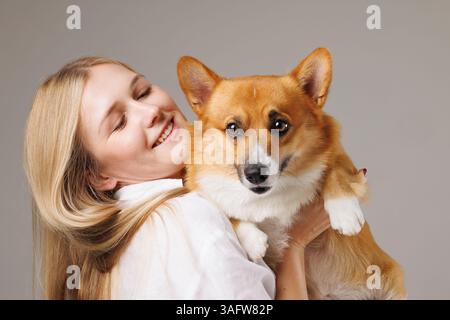 Giovane donna gioiosa che tiene in braccio il suo adorabile cane Corgi, sia felice che affettuoso, in un primo piano. Foto Stock