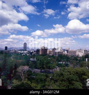 Blick auf die Skyline von Mexiko-Stadt, CA. 1985, mit modernen Hochhäusern und dem Torre Latinoamericana im Hintergrund. Im Vordergrund erstreckt sich ein Großer Park mit dichtem Grün. Foto Stock