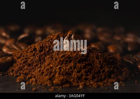Macina di un chicco di caffè in una montagna di caffè macinato, su sfondo nero. Foto Stock