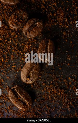 Immagine verticale dall'alto con primi piani di chicchi di caffè su sfondo scuro con caffè macinato Foto Stock