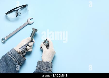 Mani del meccanico con bullone, dado, chiave e occhiali protettivi su sfondo blu Foto Stock