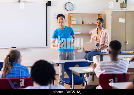 Presentazione del progetto a scuola, ragazzo che tiene un tablet mentre un'insegnante indiana e gli studenti guardano Foto Stock