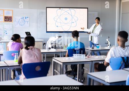 A scuola, insegnante donna indiana che presenta il diagramma scientifico sullo schermo agli studenti in classe Foto Stock