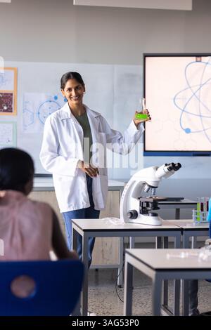 A scuola, insegnante indiana che tiene la fiasca e spiega agli studenti l'esperimento scientifico Foto Stock