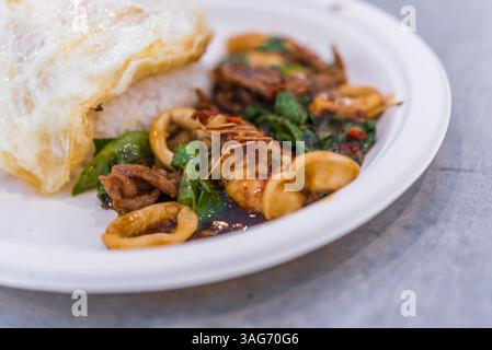 Riso condito con maiale fritto in padella o manzo con fegato, calamari e basilico in vendita al mercato o al ristorante Thai Street food di Bangkok in Thailandia Foto Stock