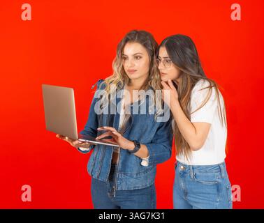 Due donne imprenditrici che utilizzano un notebook su sfondo rosso, donne professionali che cercano qualcosa online pensando, leggendo la navigazione Foto Stock