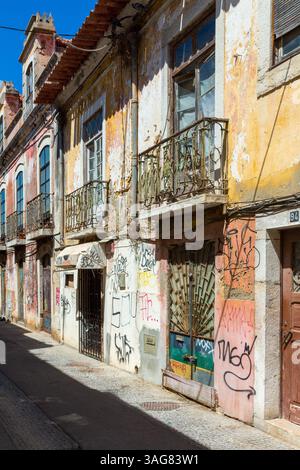 Facciata dell'edificio con graffiti e colori sbucciati in una stretta strada di Lisbona, che mostra il decadimento urbano e il fascino. Foto Stock