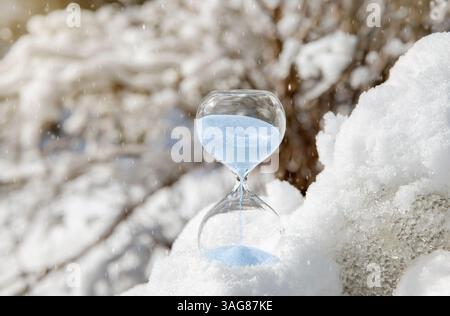 Immagine concettuale del passaggio all'ora invernale o all'inversione di marcia, fine dell'ora legale. Attenzione selettiva alla clessidra con sabbia blu che cade. Foto Stock