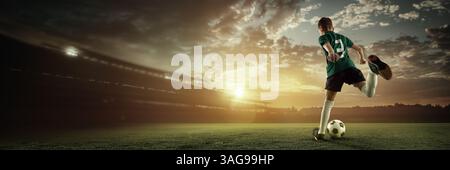 La vista posteriore del ragazzo con la maglia verde si ritrova in un'azione potente al tramonto su un campo da calcio incandescente. Rendering 3D di un'arena all'aperto. Foto Stock