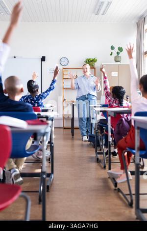 Coinvolgere studenti diversi in classe, insegnante donna alzando la mano e partecipando alla scuola Foto Stock