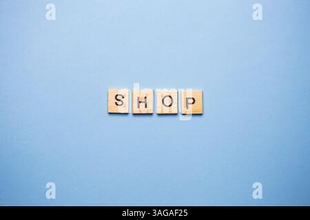 Le piastrelle in legno scrivono la parola "SHOP" su uno sfondo azzurro. Foto Stock
