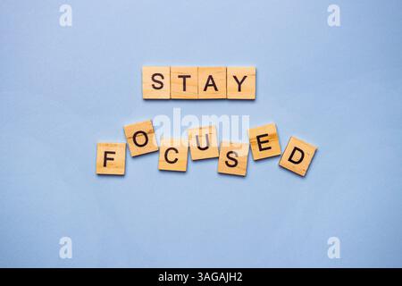 Le tessere in legno scrivono il messaggio motivazionale "Mantieni la concentrazione" su uno sfondo azzurro. Foto Stock