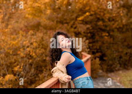 Donna spensierata appoggiata su una rotaia con gli occhi chiusi e gode di una splendida giornata autunnale all'aperto Foto Stock