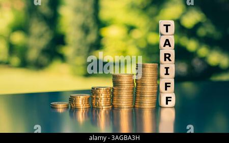 I dadi formano la parola Tariff accanto all'aumento di alte pile di monete. Simbolo delle crescenti tariffe statunitensi sulle merci internazionali. Foto Stock