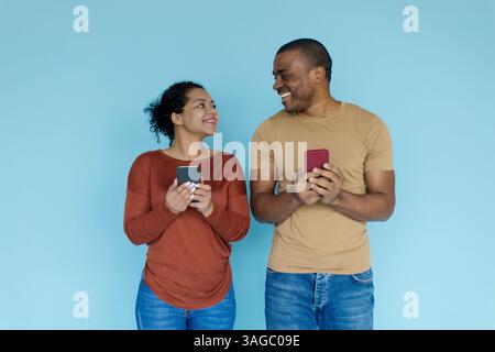 Ottima app. Felice coppia nera che tiene gli smartphone e si guarda l'un l'altro Foto Stock