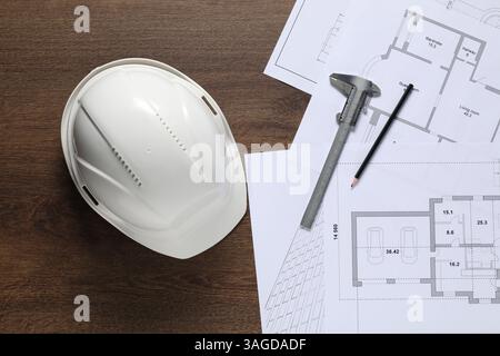 Diversi disegni architettonici, elmetto, matita e calibro a corsoio su tavolo in legno, piatto Foto Stock