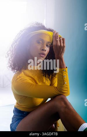 Donna sicura di sé con la parte superiore gialla che posa con cura in un elegante ambiente da studio. Moda, fiducia, moderno, ritratto, creativo, espressione Foto Stock