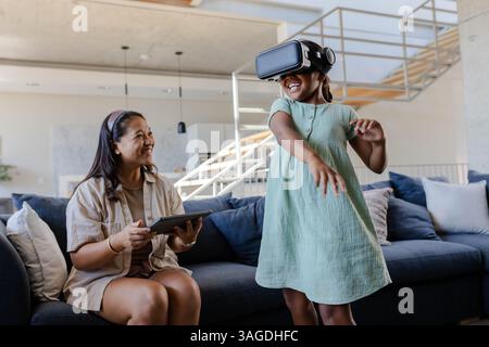 Madre e figlia si divertono a giocare in realtà virtuale a casa, condividendo momenti di gioia. Famiglia, bonding, tecnologia, vr, gaming, felicità Foto Stock