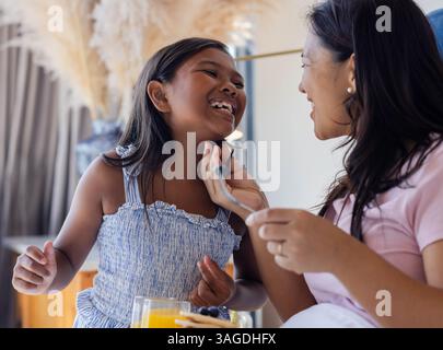 Madre e figlia ridono insieme mentre si gustano la colazione a casa. Famiglia, Unione, legame, felicità, mattina, pasto Foto Stock
