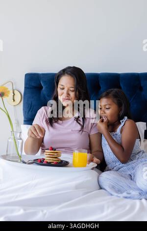 Madre e figlia si godevano la colazione a letto con pancake e succo di frutta. Famiglia, legame, mattina, relax, felicità, accogliente Foto Stock